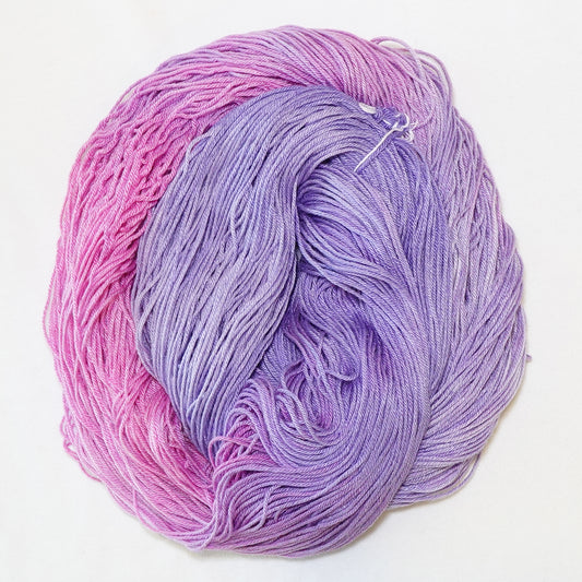 Hand-dyed fingering weight yarn in petal pink and soft lilac with a soft tonal fade.