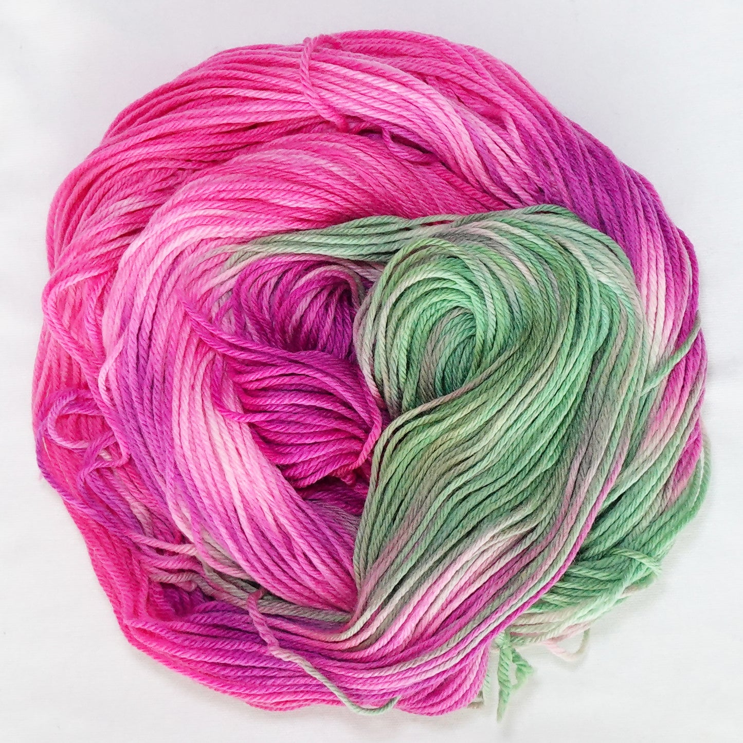 Hand-dyed worsted weight yarn in vivid magenta, soft pink, sage green, and white.