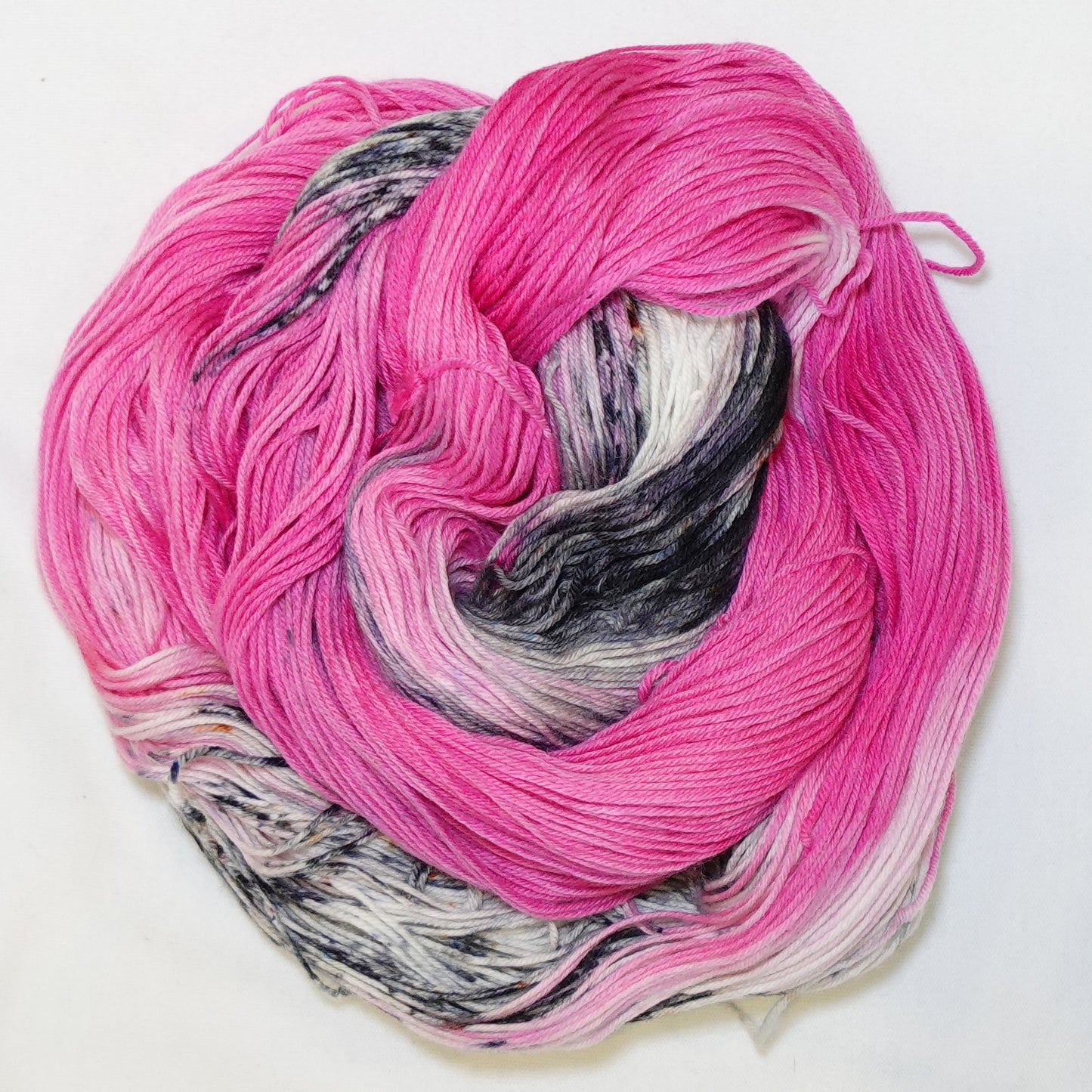 Hand-dyed fingering weight yarn in hot fuchsia pink with black, white, and grey speckled sections throughout.