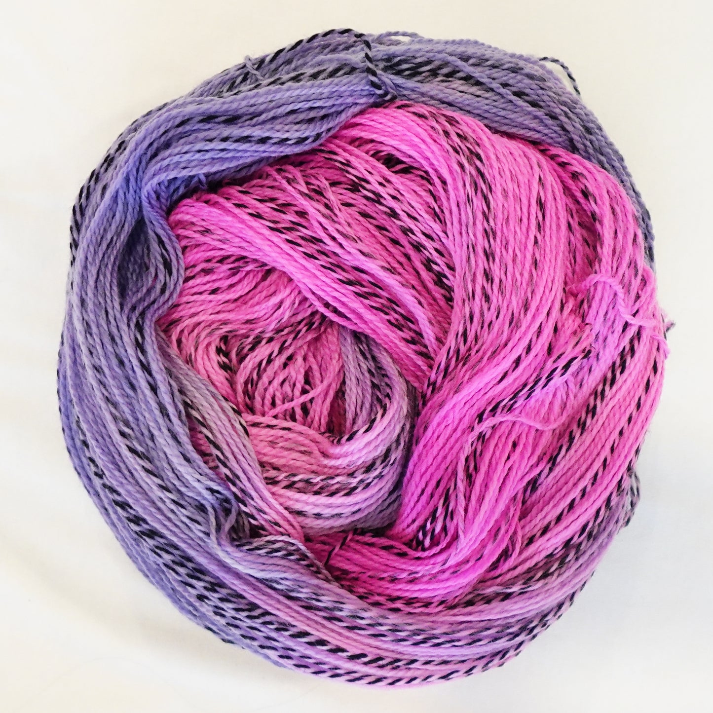 Hand-dyed fingering weight yarn in hot pink and soft lilac with black twisted through and a muted orchid blend where the colors meet.