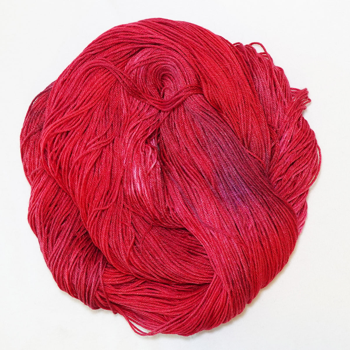 Hand-dyed fingering weight yarn in deep jeweled red with soft violet tones throughout.