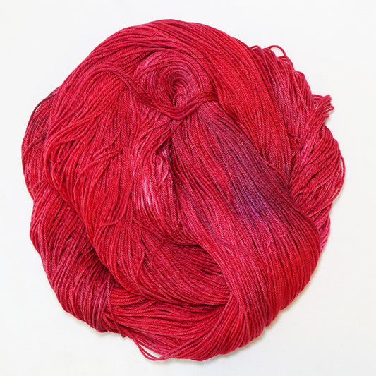 Hand-dyed fingering weight yarn in deep jeweled red with soft violet tones throughout.