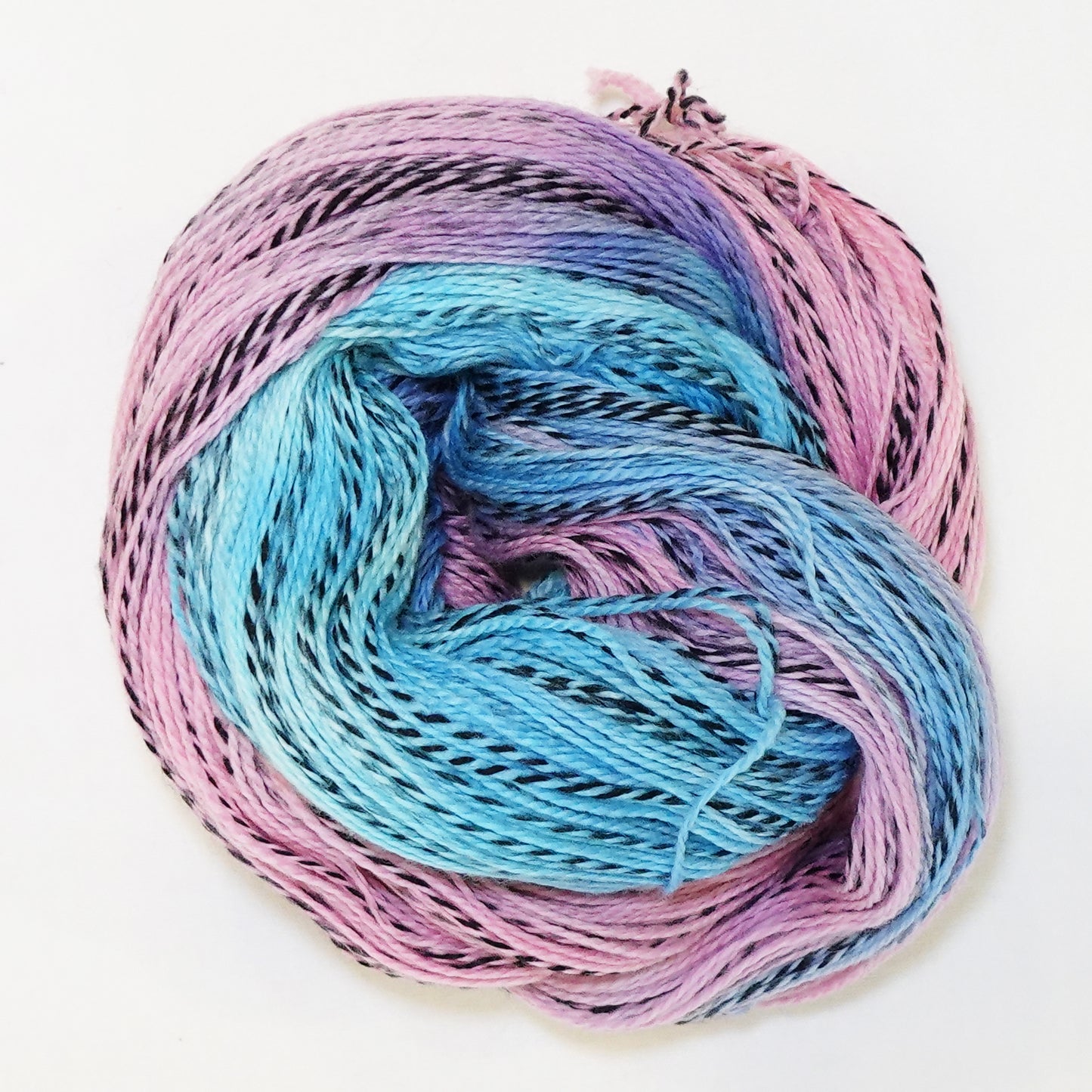Hand-dyed fingering weight yarn in soft sky blue and rose pink with black twisted through and a hazy lavender where the colors meet.