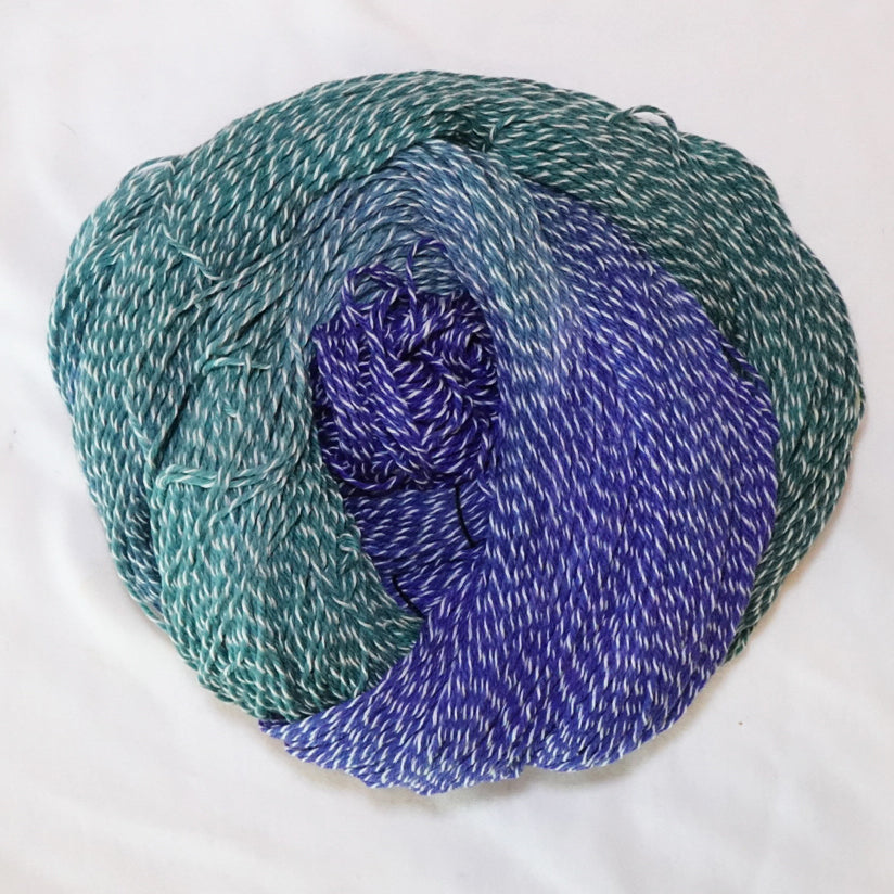 Hand-dyed fingering weight yarn in sea glass teal, misty aqua, and royal blue with white twisting through.