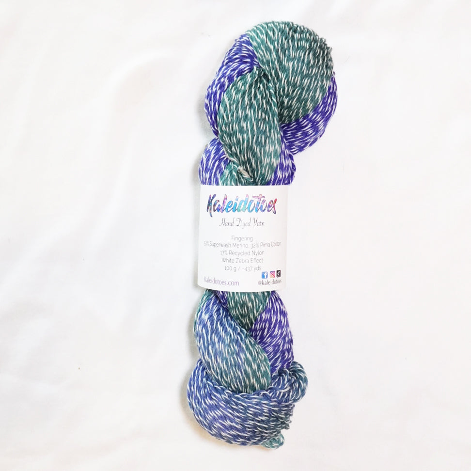 Hand-dyed fingering weight yarn in sea glass teal, misty aqua, and royal blue with white twisting through.