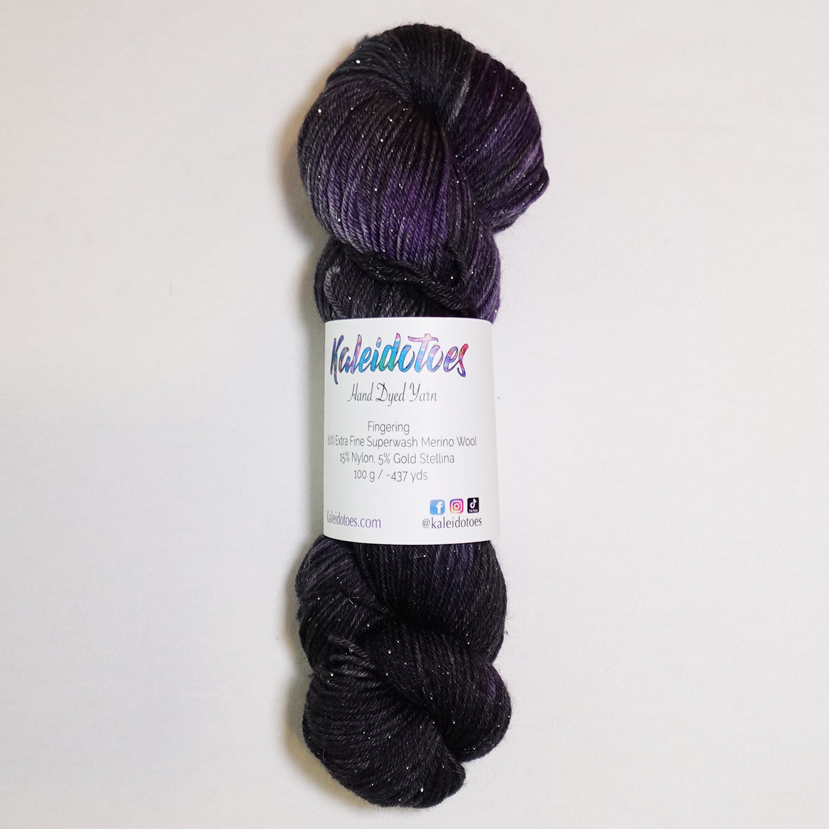 Hand-dyed gold metallic fingering weight yarn in near-black, smoky charcoal and deep violet with a fine gold metallic thread.