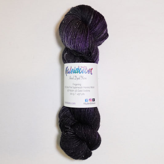 Hand-dyed gold metallic fingering weight yarn in near-black, smoky charcoal and deep violet with a fine gold metallic thread.