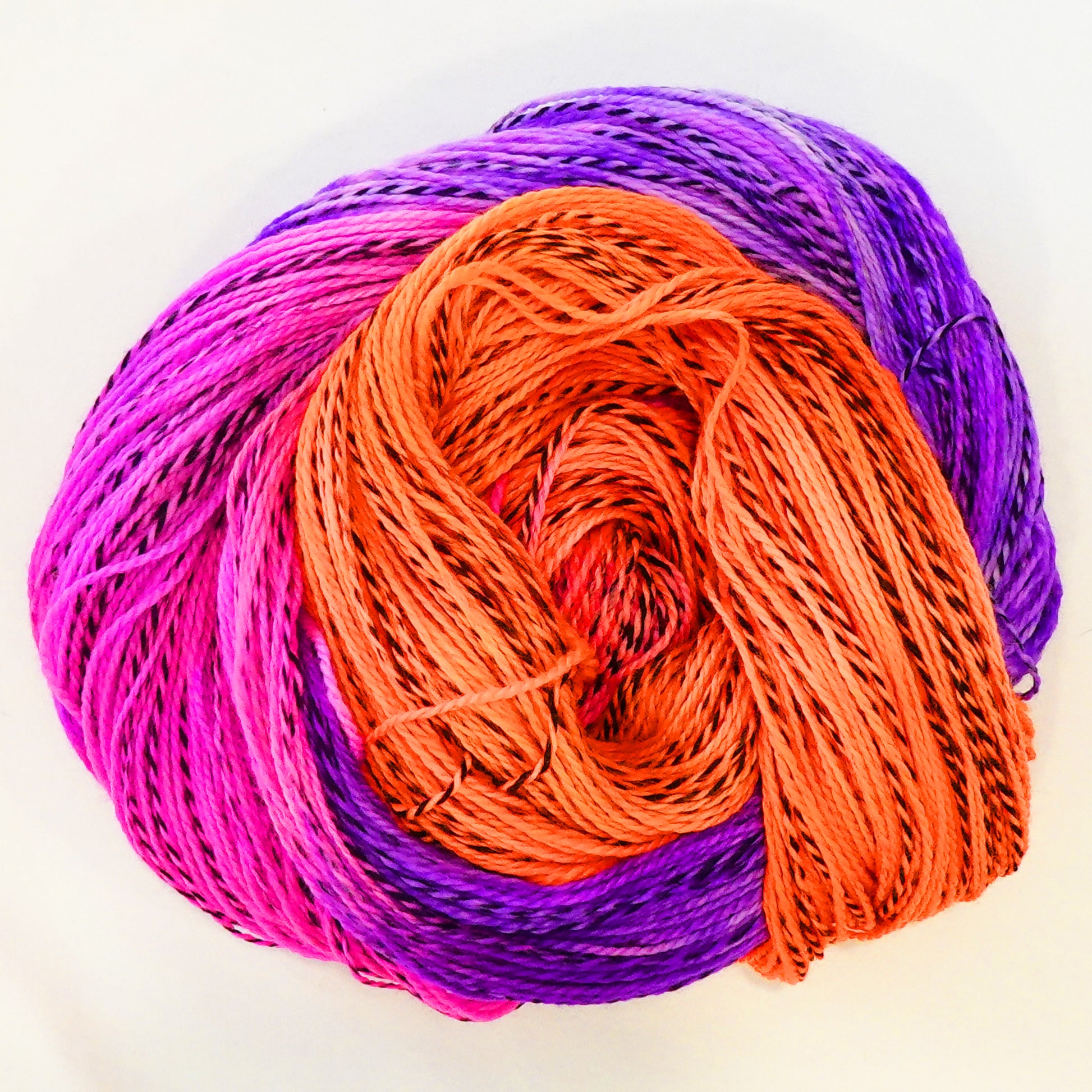 Hand-dyed fingering weight yarn in fluorescent orange, hot magenta, and rich purple with black threading throughout on a zebra base.