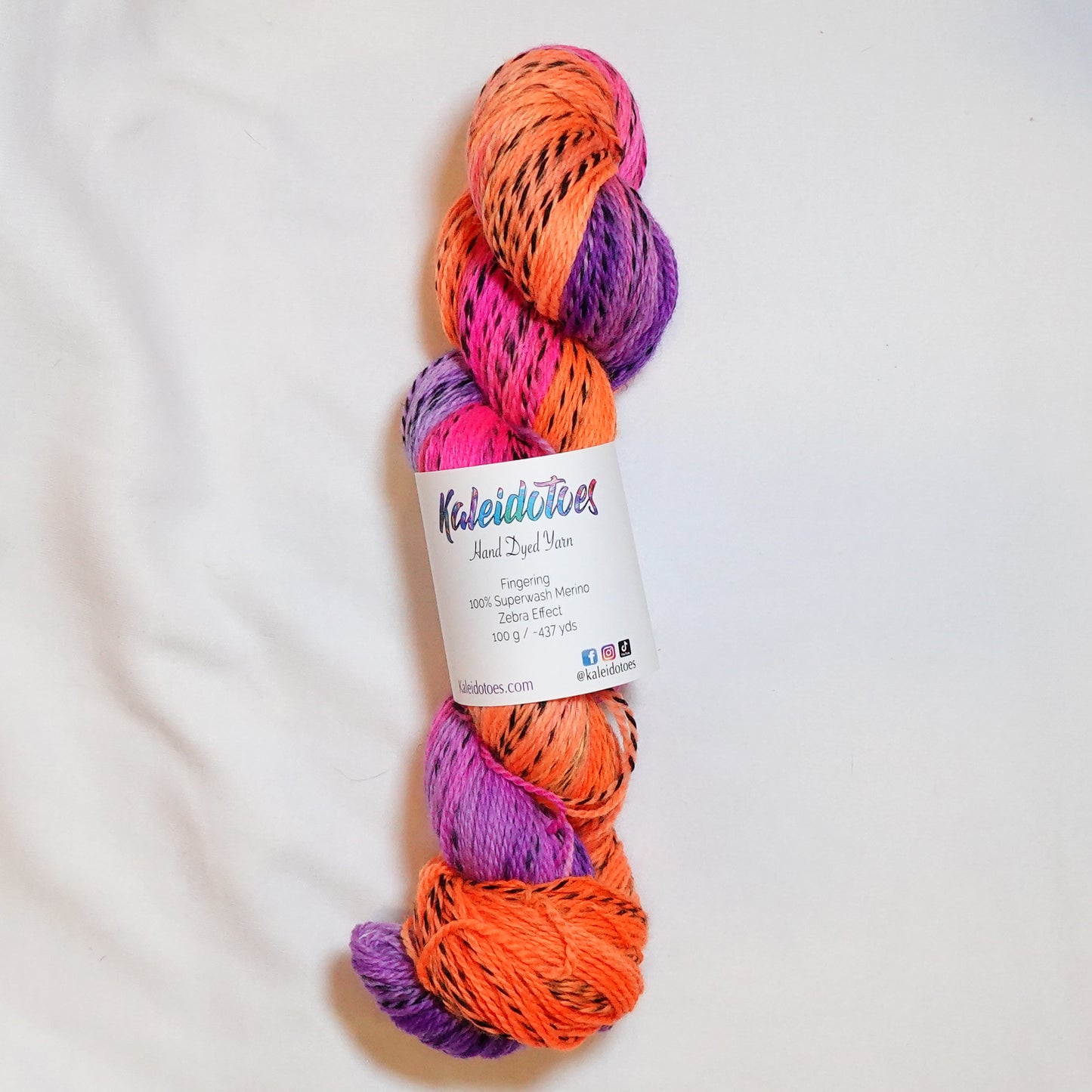 Hand-dyed fingering weight yarn in fluorescent orange, hot magenta, and rich purple with black threading throughout on a zebra base.