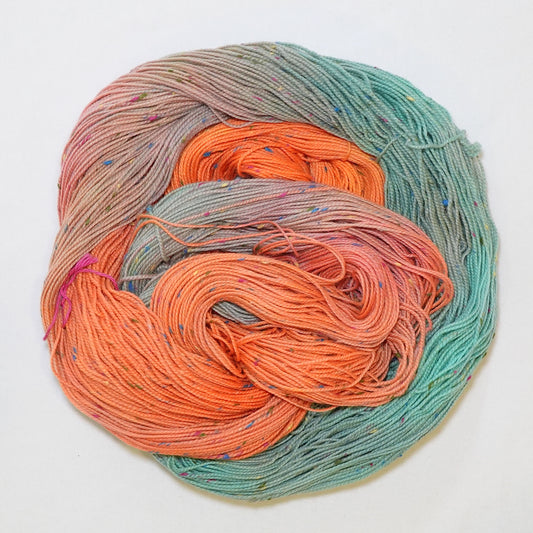 Hand-dyed fingering weight yarn in coral, seafoam, and blush with multicolor confetti flecks throughout.