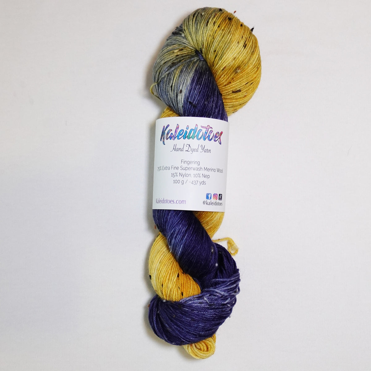 Hand-dyed tweed fingering weight yarn in golden yellow, deep blue-violet, navy and smoky blue-grey with black tweed flecks.