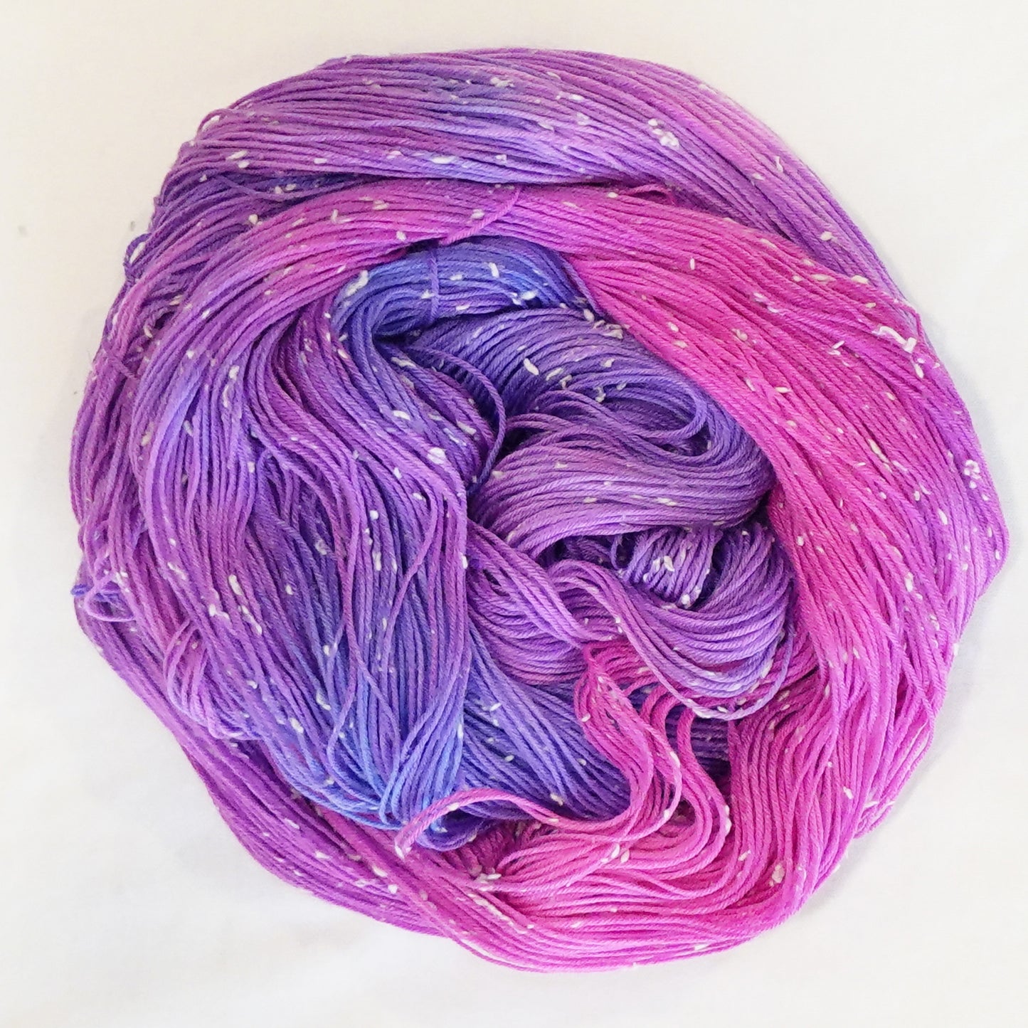 Hand-dyed yarn in vibrant violet, lavender, and bright pink tones with soft white flecks — playful, bold, and full of movement.