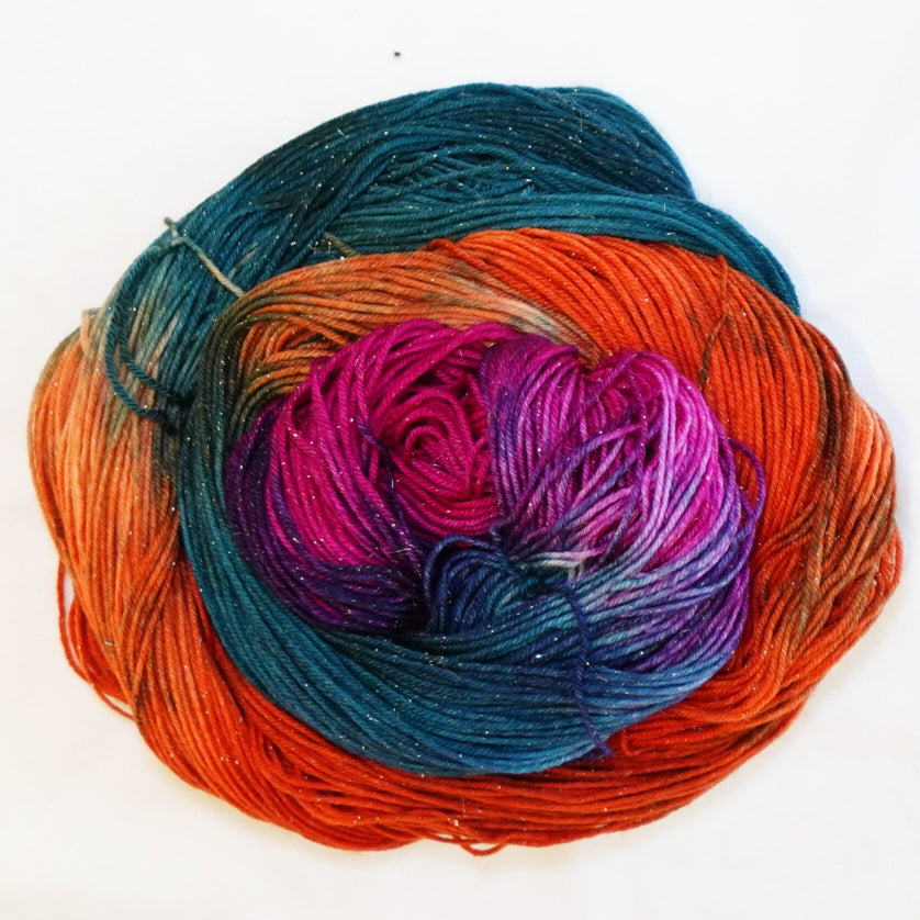 Hand-dyed gold metallic fingering weight yarn in fiery orange, deep teal, brilliant magenta and violet with a fine gold metallic thread.