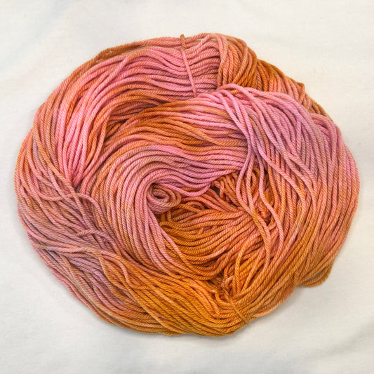 Hand-dyed yarn in shades of peach, golden amber, and blush pink — glowing softly like a sunset sky.