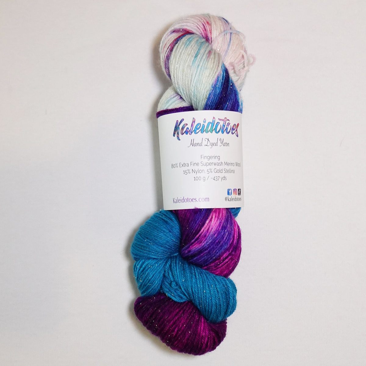 Hand-dyed gold metallic fingering weight yarn in magenta, vivid violet and turquoise with white accents and a fine gold metallic thread.