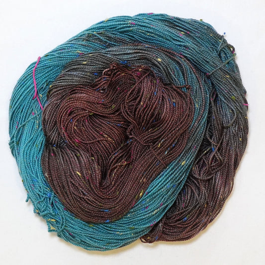 Hand-dyed fingering weight yarn in deep chocolate and bright teal with charcoal transitions and multicolor confetti flecks throughout.