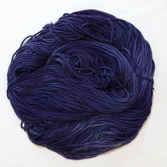 Hand-dyed worsted weight yarn in deep washed indigo blue-violet tones with soft, diffused tonal variation and near-white patches throughout.