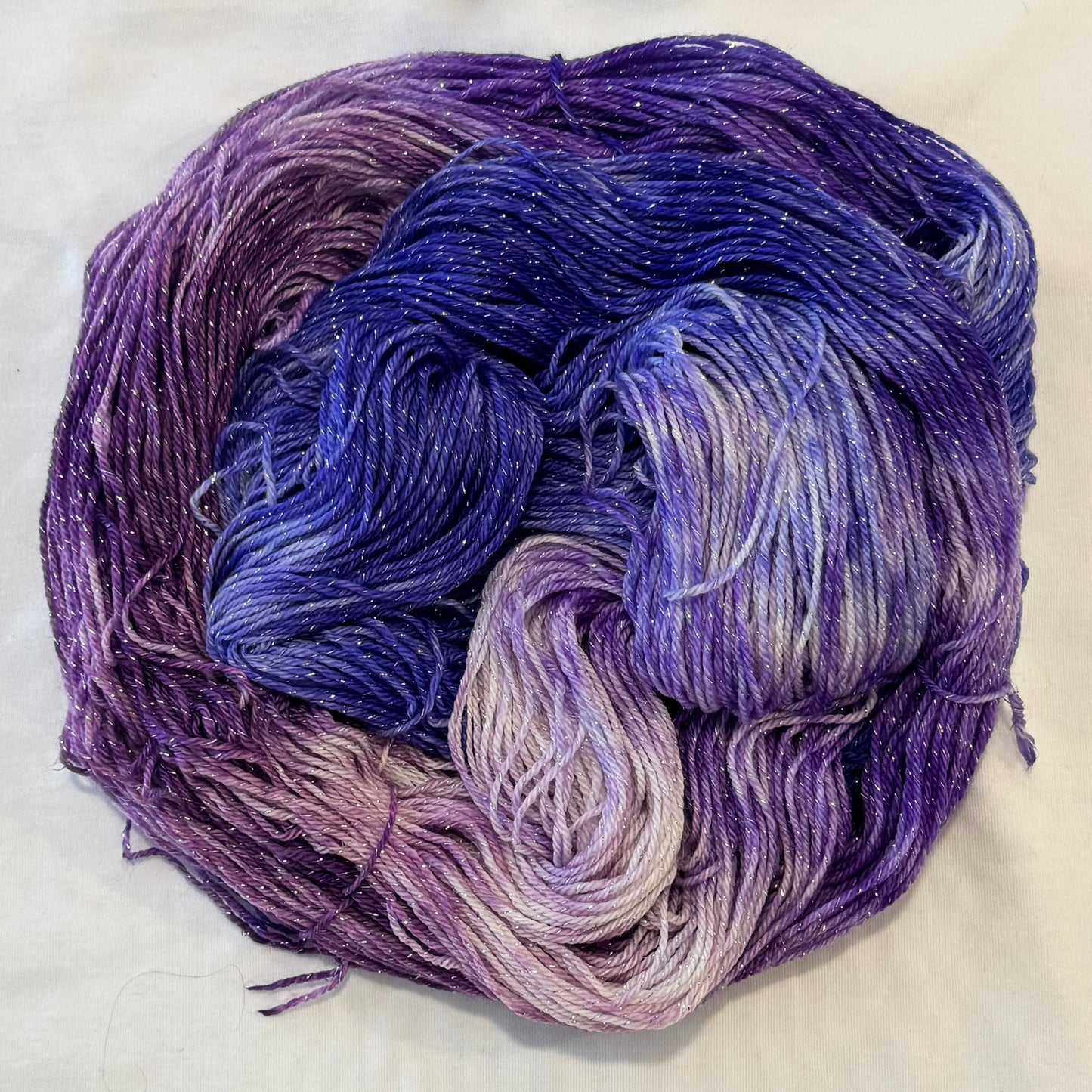 Hand-dyed yarn in grape, berry, lilac, and violet tones with subtle silver metallic throughout.