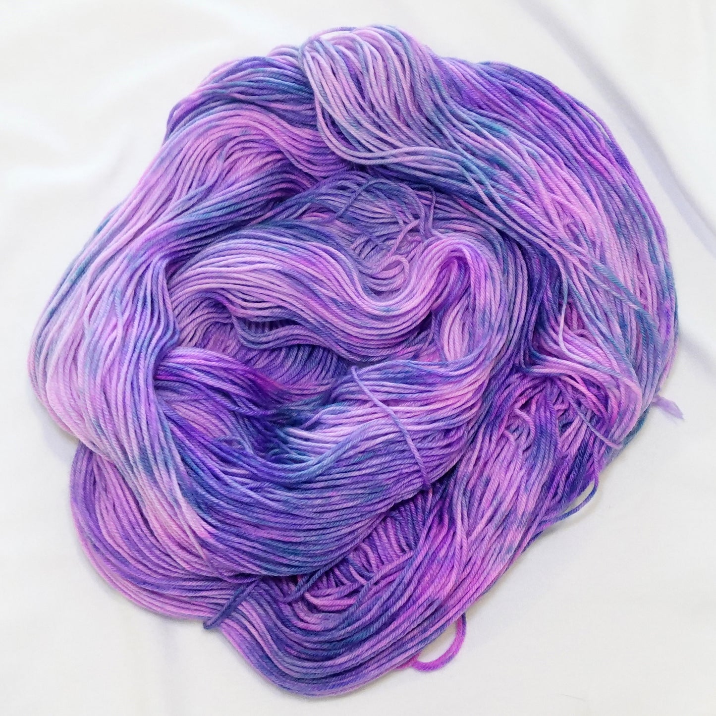 Hand-dyed fingering weight yarn in lavender, orchid, violet, and cool periwinkle with flowing variegated movement.