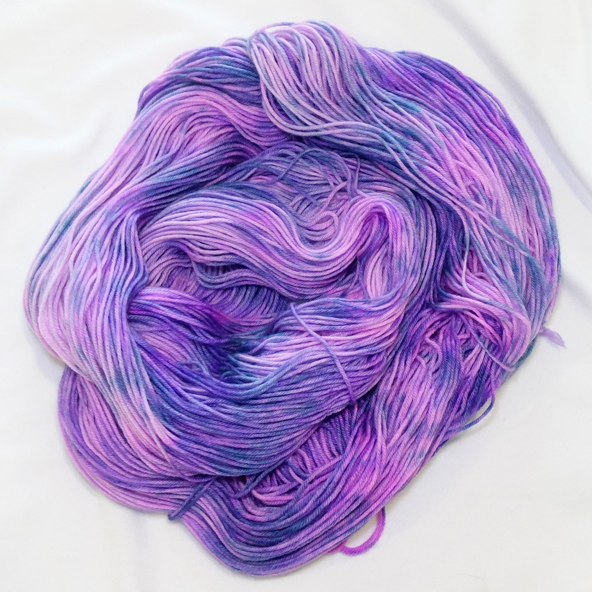 Hand-dyed fingering weight yarn in lavender, orchid, violet, and cool periwinkle with flowing variegated movement.