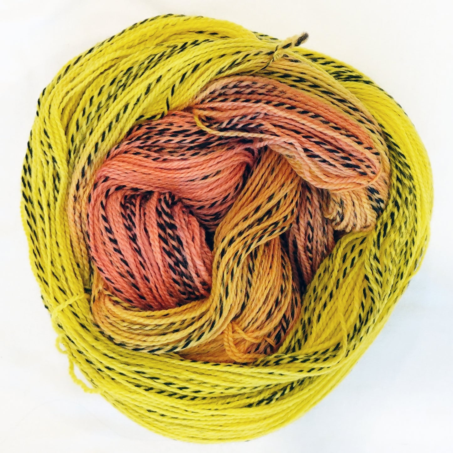 Hand-dyed fingering weight yarn in bright lemon yellow, warm peach, and coral with black twisted through throughout.