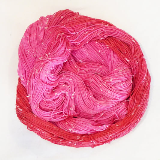 Hand-dyed yarn in vibrant pink and berry red tones with soft white flecks — bright, juicy, and playful.
