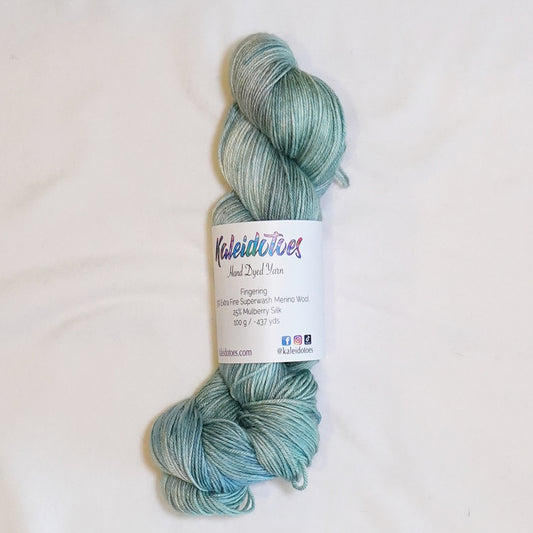 Hand-dyed fingering weight yarn in soft blue-green, dusty sage, pale aqua, and silvery gray tones.