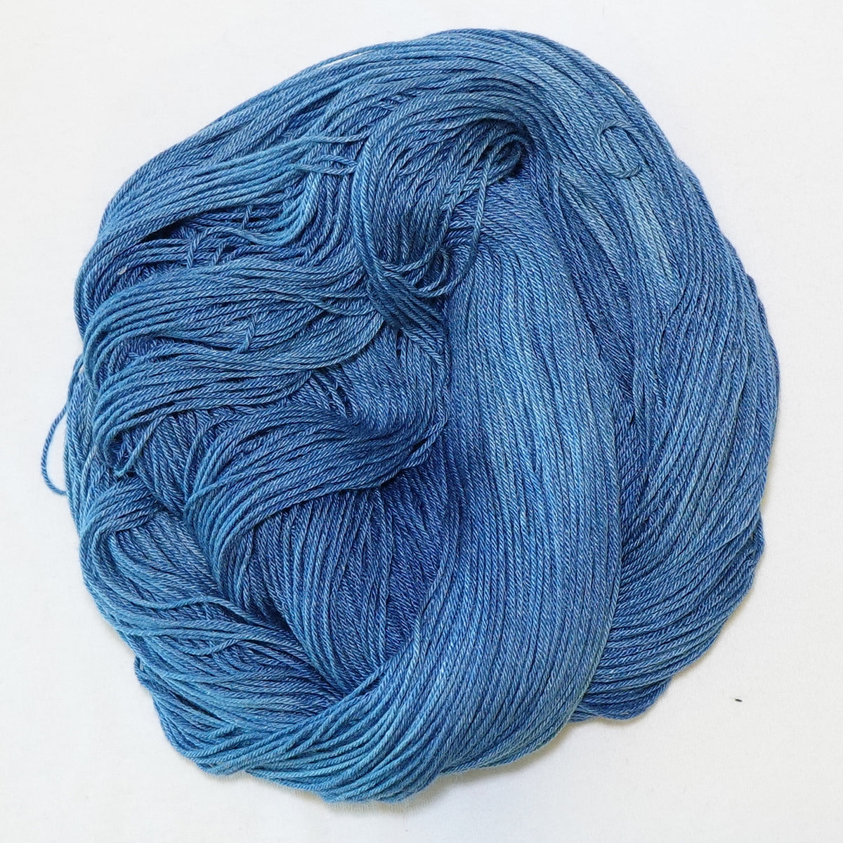 Hand-dyed fingering weight yarn in faded denim blue with lighter worn tones and deeper indigo throughout.