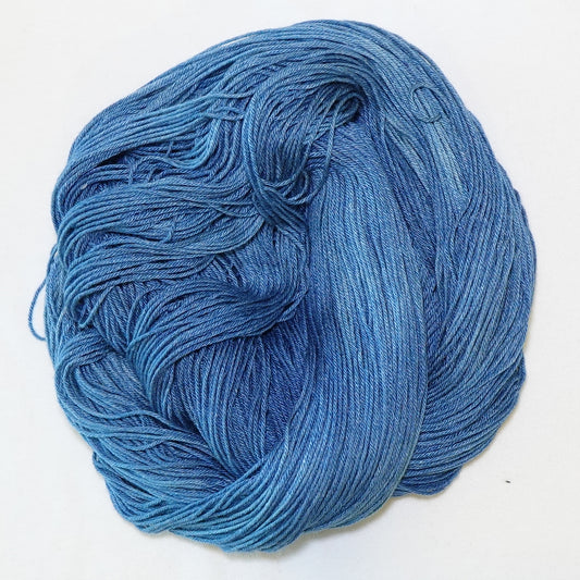 Hand-dyed fingering weight yarn in faded denim blue with lighter worn tones and deeper indigo throughout.