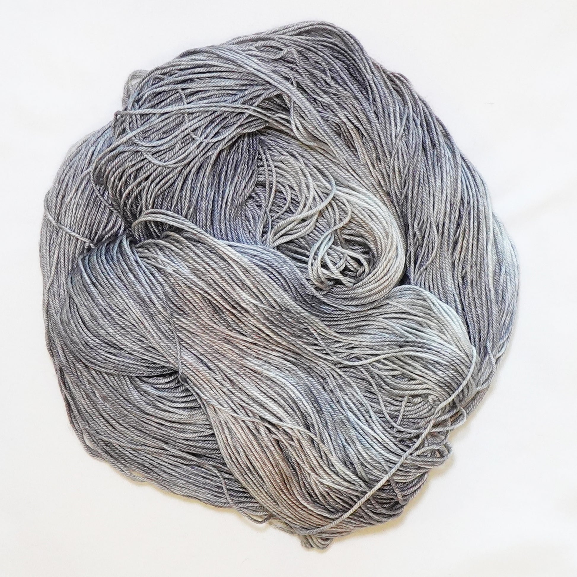 Hand-dyed fingering weight yarn in weathered stone gray, pale blue-gray, soft taupe, and dusty fawn tones.