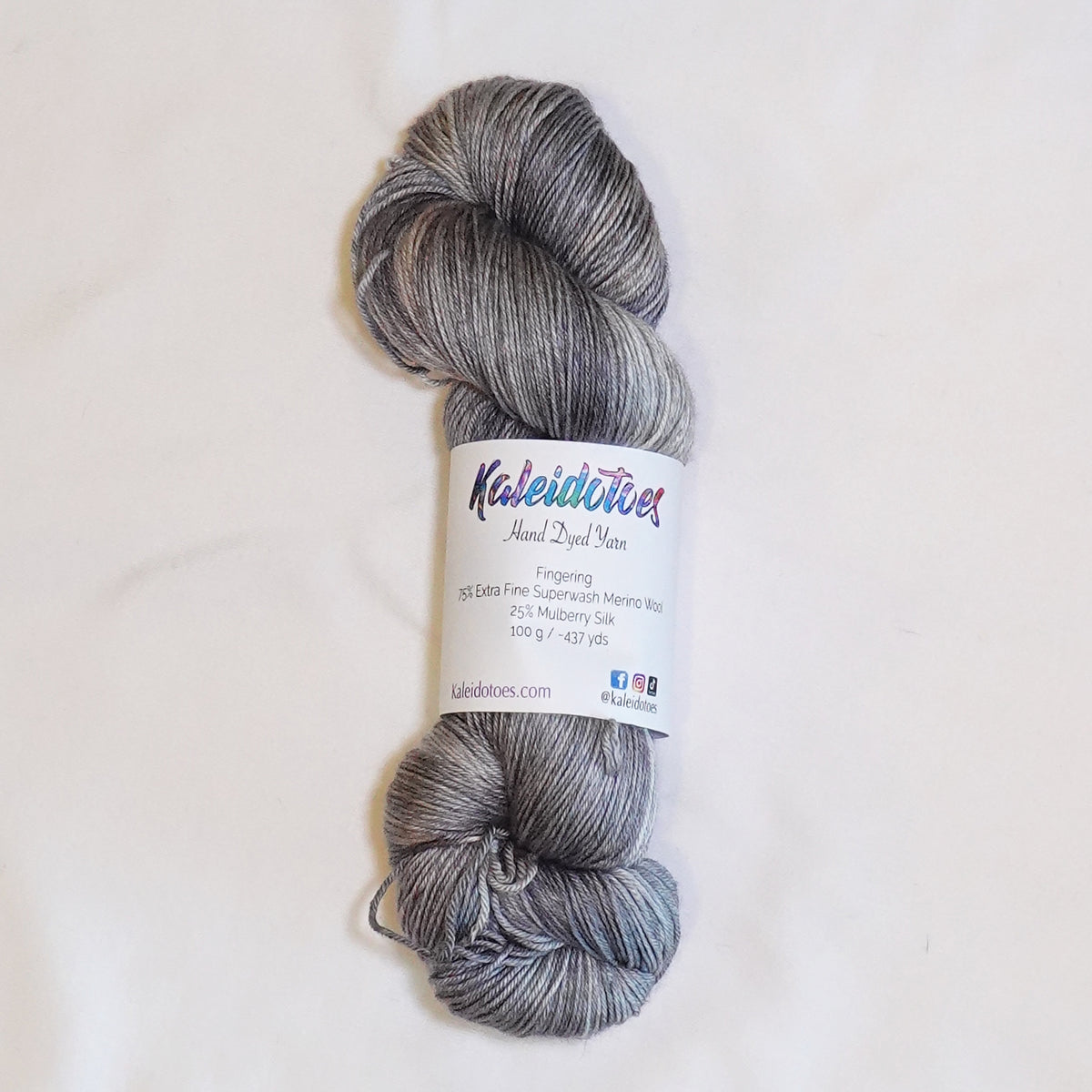 Hand-dyed fingering weight yarn in weathered stone gray, pale blue-gray, soft taupe, and dusty fawn tones.