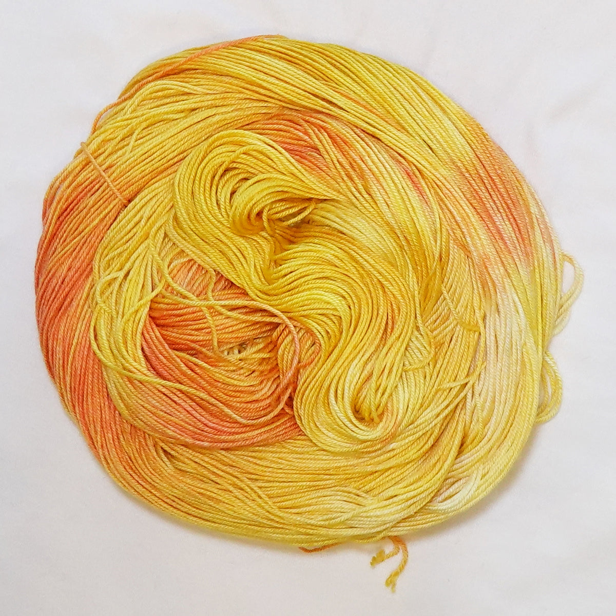Hand-dyed fingering weight yarn in golden yellow, warm apricot, buttery yellow, and soft orange tones.