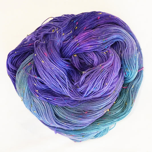 Hand-dyed yarn in violet and blue tones with colorful flecks — vibrant, dynamic, and reminiscent of confetti in a night sky.