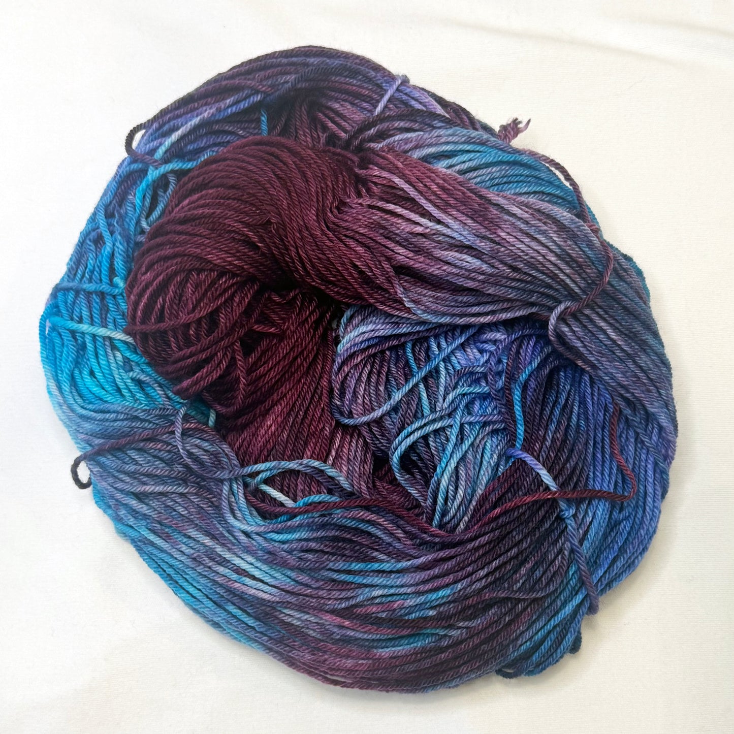 Hand-dyed yarn in shades of cranberry, turquoise, indigo, and soft white — luminous and richly blended with a cosmic glow.