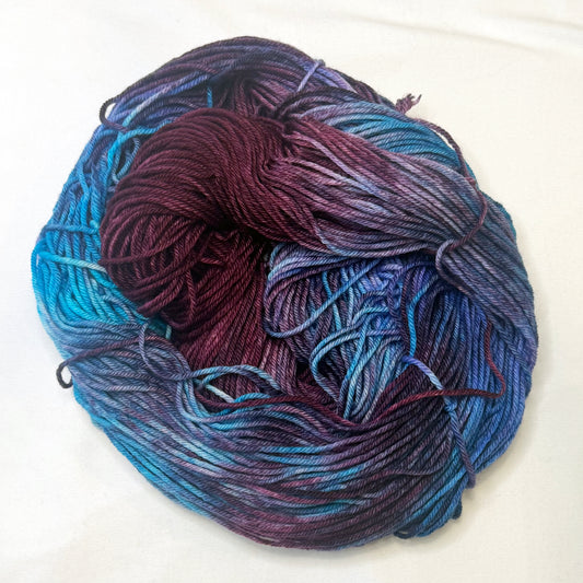 Hand-dyed yarn in shades of cranberry, turquoise, indigo, and soft white — luminous and richly blended with a cosmic glow.