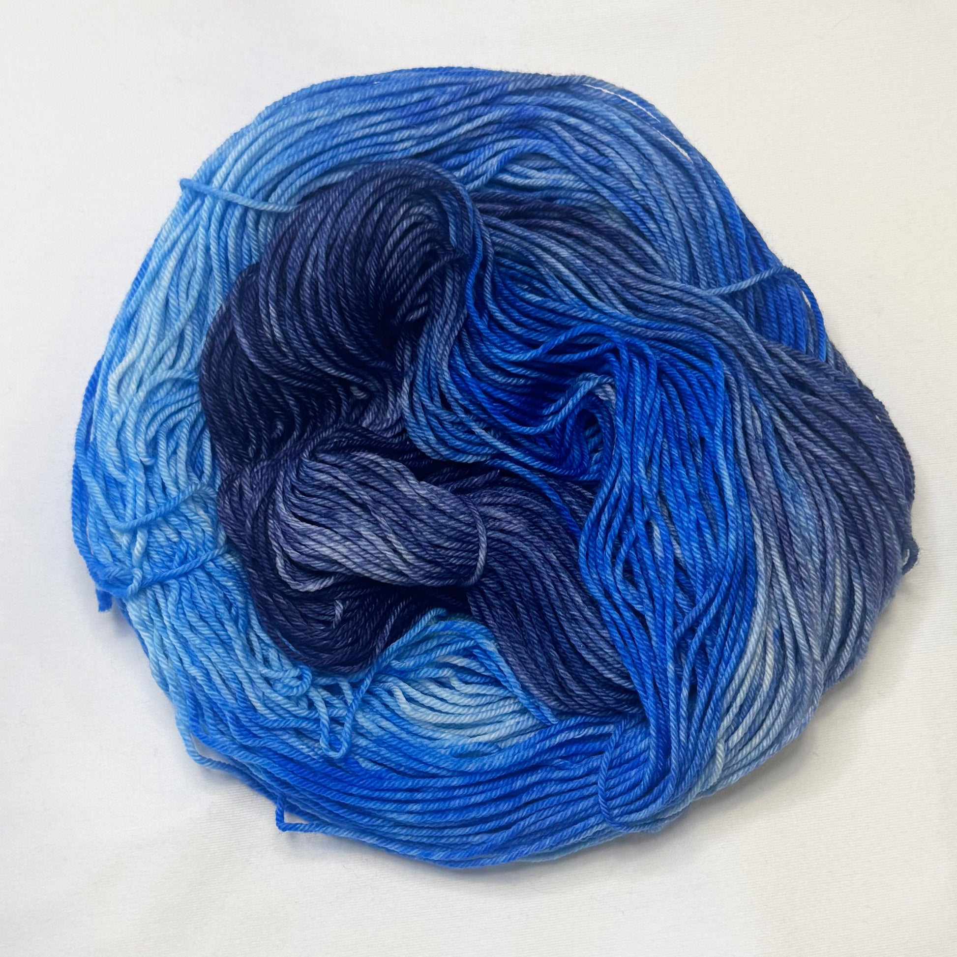 Hand-dyed yarn in deep navy, electric blue, cool blue, and soft white — a luminous blend inspired by moonlight on rippling water.