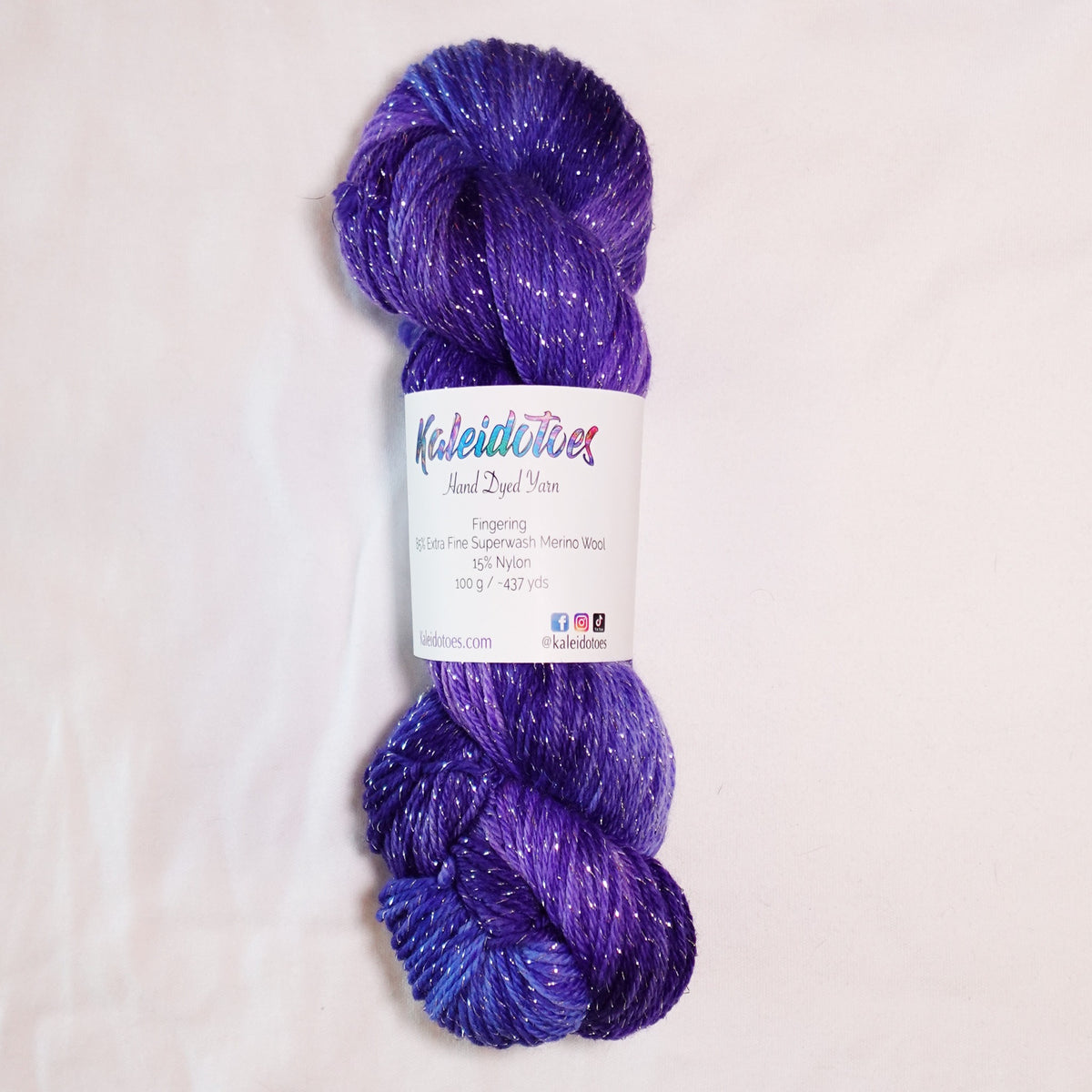 Electric Socialite hand-dyed silver metallic fingering weight yarn skein in deep violet, lilac, and dark periwinkle with silver sparkle.