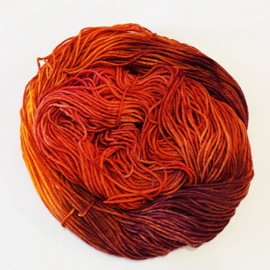 Hand-dyed yarn skein in layered orange tones with hints of gold and deeper cabernet shades