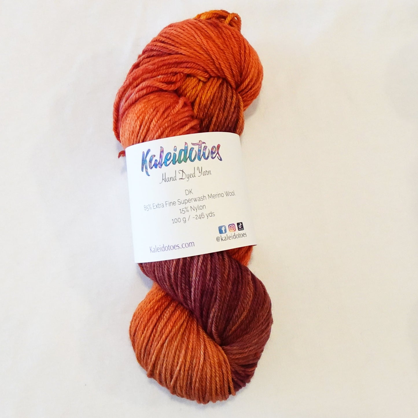 Hand-dyed yarn skein in layered orange tones with hints of gold and deeper cabernet shades