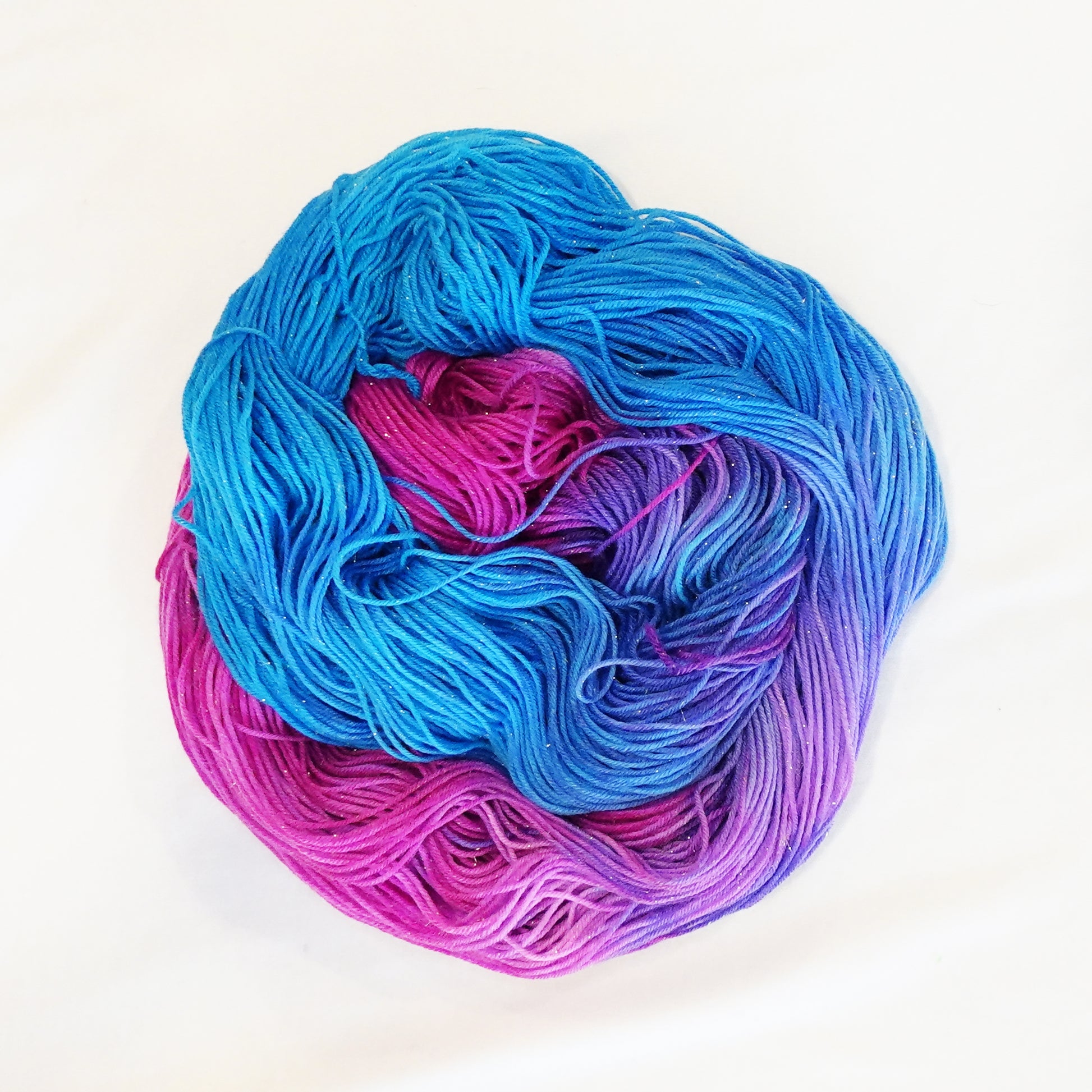 Hand-dyed yarn in vibrant blue, pink, and violet tones with gold metallic running throughout — bright, whimsical, and full of movement.