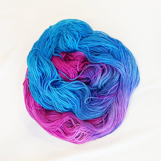 Hand-dyed yarn in vibrant blue, pink, and violet tones with gold metallic running throughout — bright, whimsical, and full of movement.
