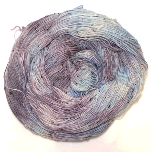 Hand-dyed tweed yarn in dusty mauve and soft grey-blue — muted, atmospheric, and quietly complex with subtle flecks throughout.