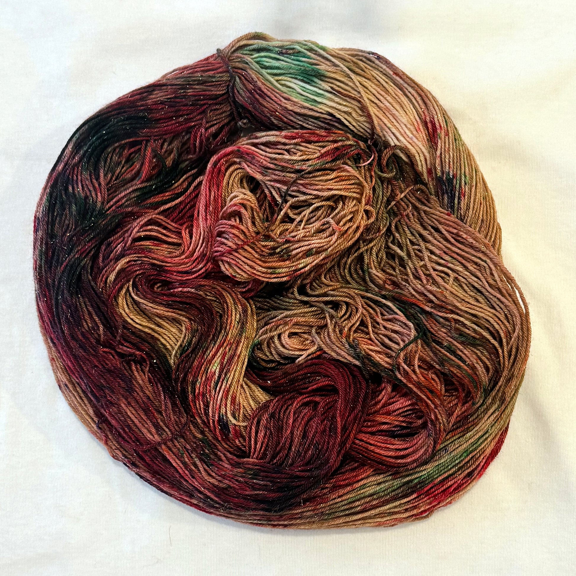 Hand-dyed yarn in warm gingerbread brown, cranberry red, caramel, evergreen, and subtle plum tones with delicate gold metallic flecks.