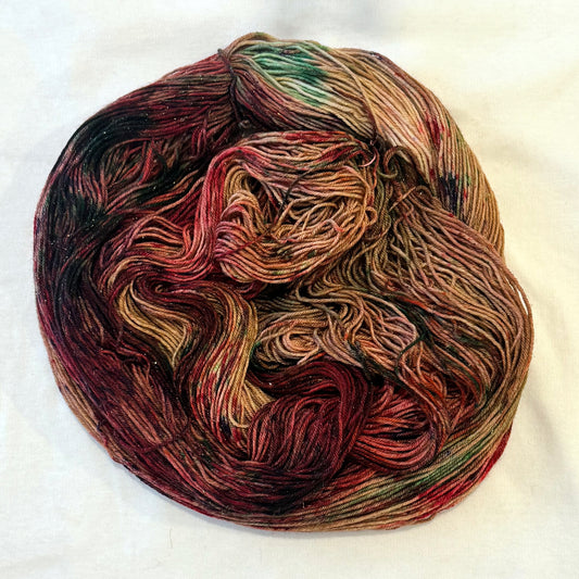 Hand-dyed yarn in warm gingerbread brown, cranberry red, caramel, evergreen, and subtle plum tones with delicate gold metallic flecks.
