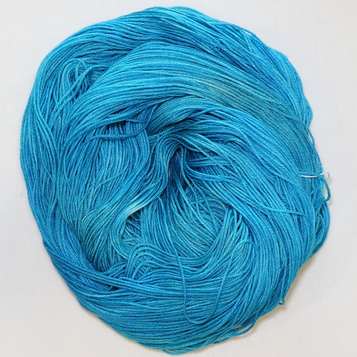 Hand-dyed fingering weight yarn in tonal turquoise blue with luminous shifts throughout.