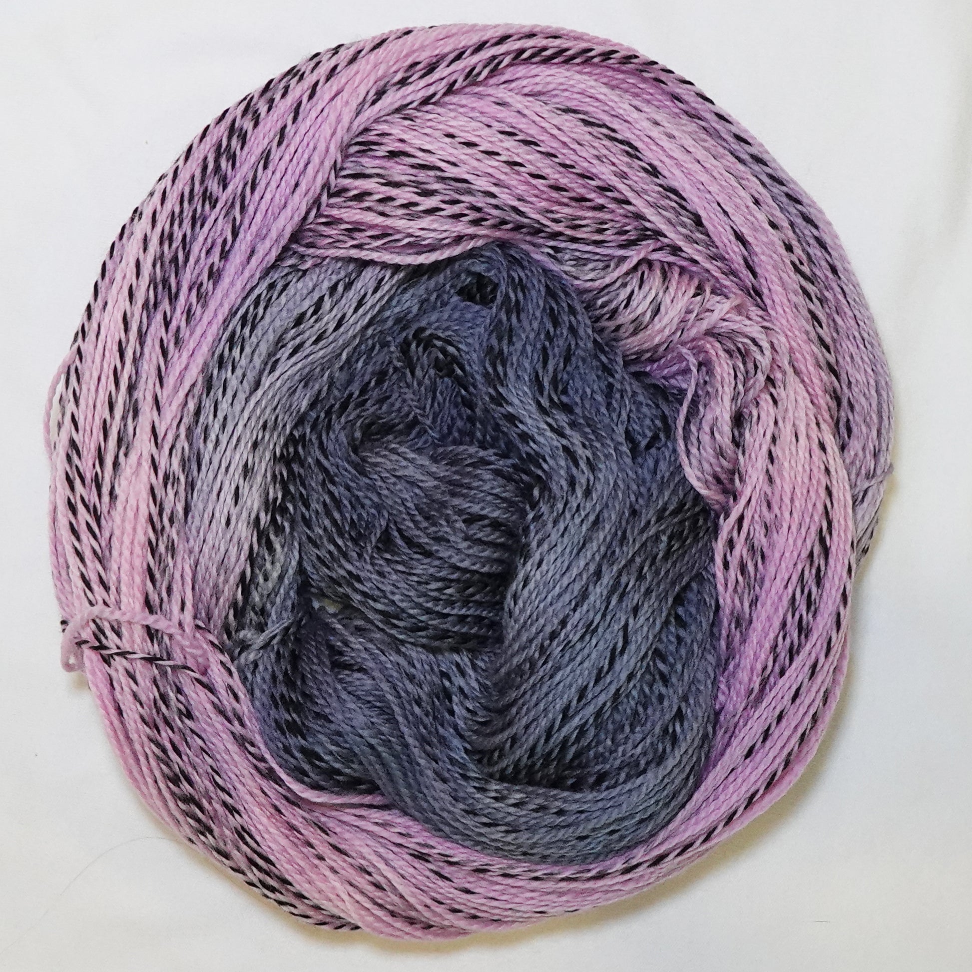 Hand-dyed fingering weight yarn in dusty pink, mauve, and deep blue-grey with black twisted through throughout.