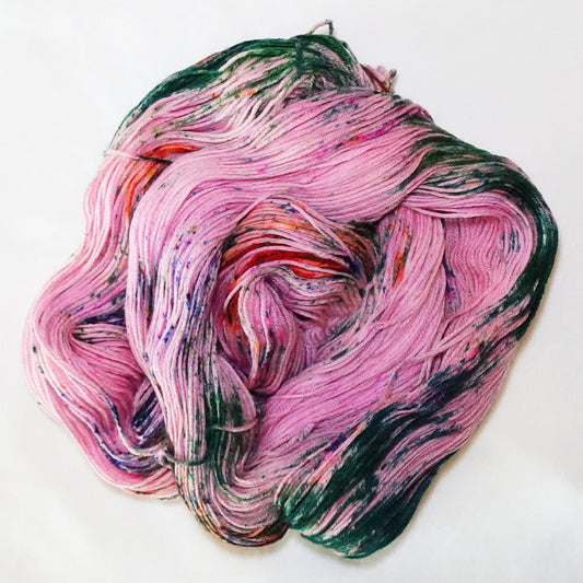 Hand-dyed fingering weight yarn in pink with deep evergreen sections and orange and violet speckles throughout.