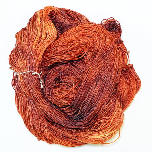 Hand-dyed fingering weight yarn in warm reddish-brown with coppery highlights and deep rust tones.