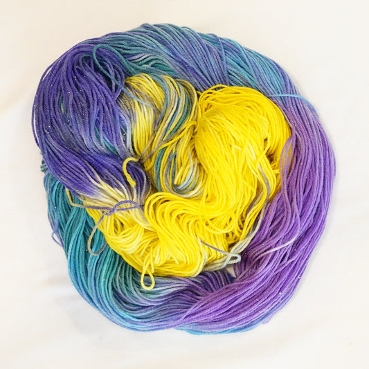 Hand-dyed yarn in shifting yellow, violet, and teal tones with gold metallic running throughout — bold, festive, and full of movement.