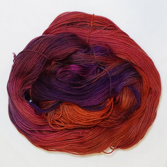 Hand-dyed fingering weight yarn in brick red, burnt orange, deep violet, and magenta with rich swirling color transitions.